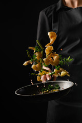 Chef cooks seafood, fry shrimps. Freezing in motion on a black photo, vertical photo