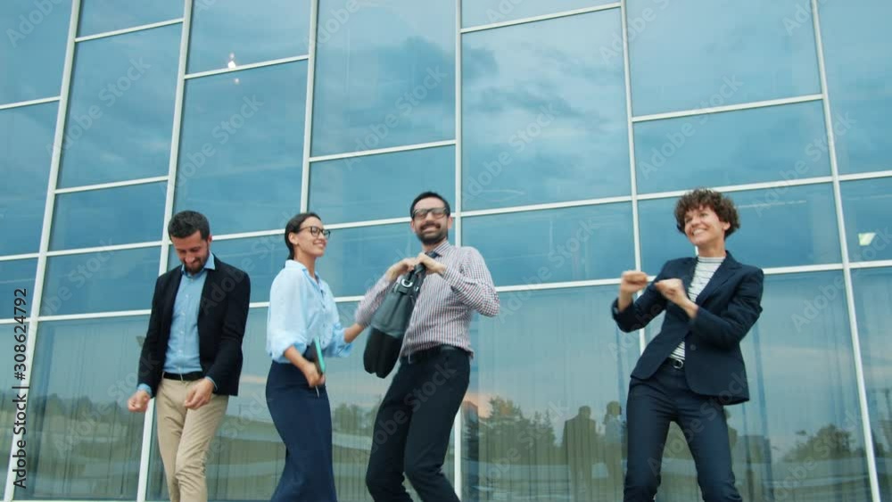 Business men and women are dancing near modern glass building outdoors relaxing feeling happy and victorious, glass wall office building is visible in background. People and fun concept. Business men and women are dancing near modern glass building outdoors relaxing feeling happy and victorious, glass wall office building is visible in background. People and fun concept.