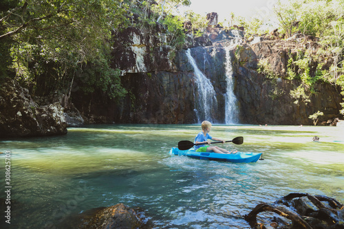 Young boy kayaking with paddle in cool blue water near waterfall at Cedar Creek Falls near Airlie Beach in the Whitsundays, Queensland Australia photo