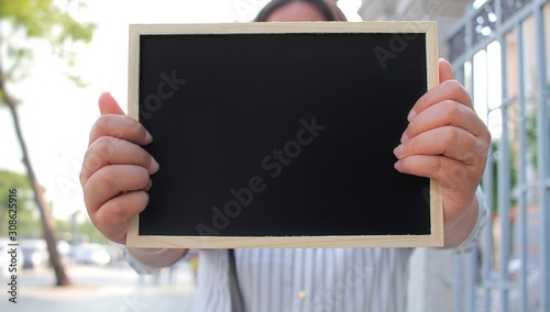 Woman with hand holding showing black chalkboard outdoor blurred background, frame composition with copy space for banner design or card and online shopping marketing or school project
