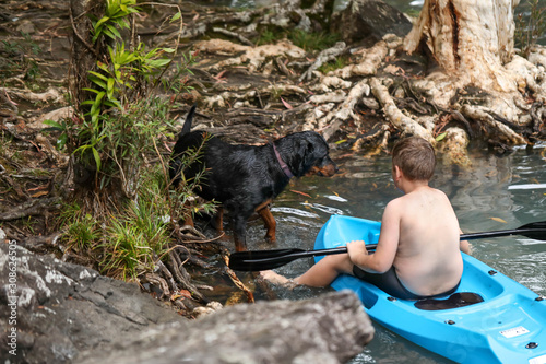 Young boy and his dog kayaking with paddle in cool blue water near waterfall at Cedar Creek Falls near Airlie Beach in the Whitsundays, Queensland Australia