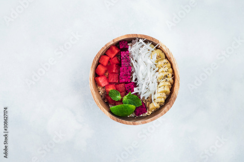 Fresh tasty smoothie bowl with dragon fruit, red watermelon, banana, coconut flakes and slice of lime. Healthy vegetarian natural breakfast. Wooden plate and light blue empty background, top view.