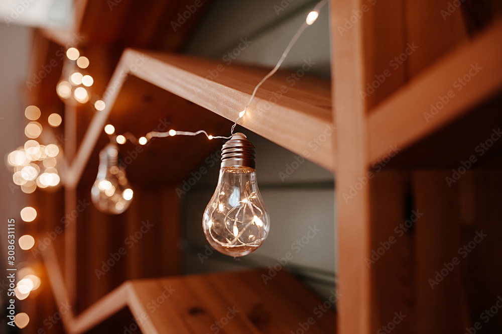 wooden shelf,shelves near the wall are decorated with garlands and one large glass bulb with light from the garland inside