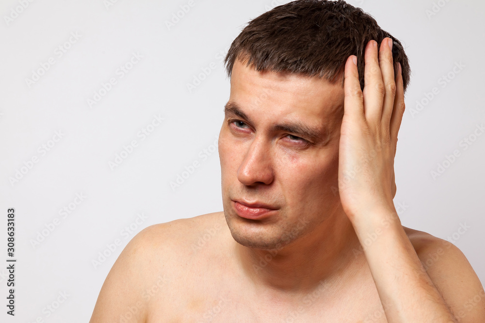 Brunette man with bruises on his body holds his hand to his head and writhes in pain on a white isolated background. Health and medicine.