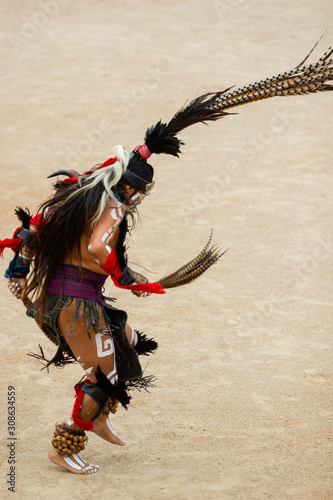 a mesoamerican dancer with bright mask, make up and feather dancing during the mesoamerican ball rubber game on a sand background