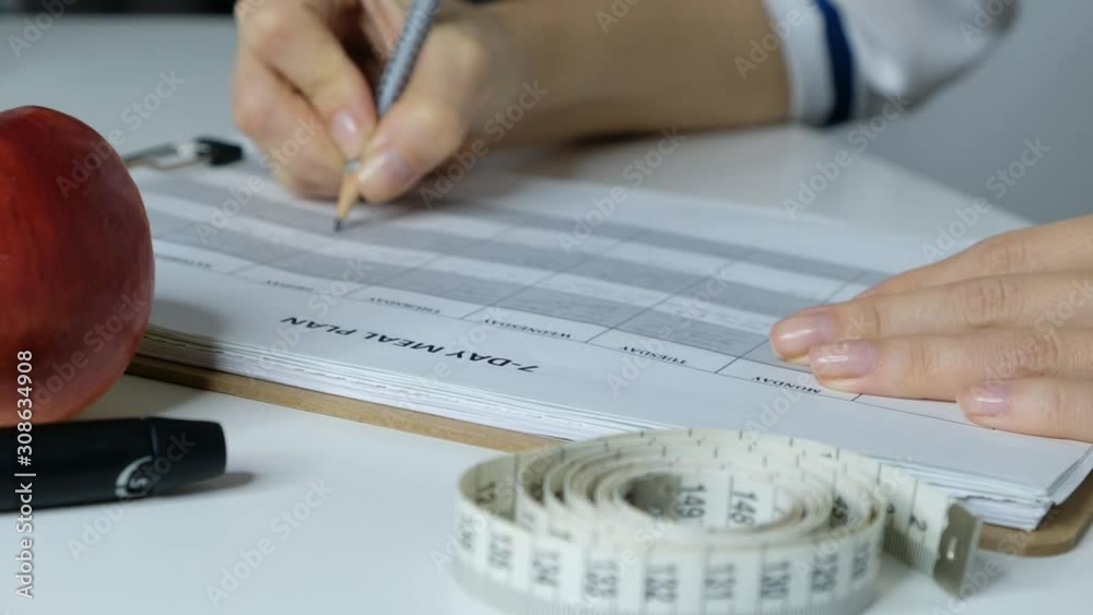 Female doctor nutritionist filling 7 day meal diet plan, close up Female doctor nutritionist filling 7 day meal diet plan, close up