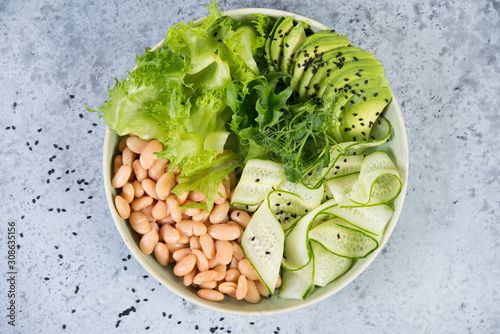 Vegetarian green salad bowl with fresh vegetables and canned white beans on a gray concrete background. Horizontal photo. Top view.