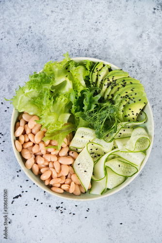 Vegetarian green salad bowl with fresh vegetables and canned white beans on a gray concrete background. Vertical photo. Top view.