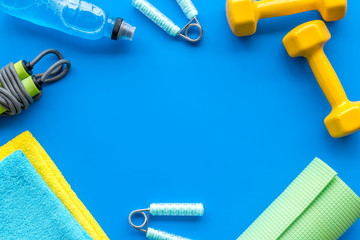 Gym equipment - dumbbells, jump rope - frame on blue background top-down copy space