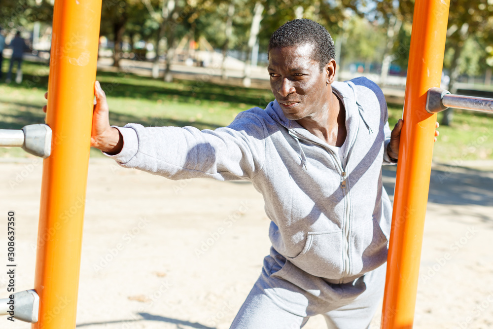 Fototapeta premium Young male training different exercises at chin-up bar in park outdoor