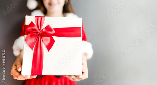 Portrait of young asian caucasian woman girl wearing santa costume and holding gift box on gray background.Young girl with smile in a Christmas costume on christmas celebration.