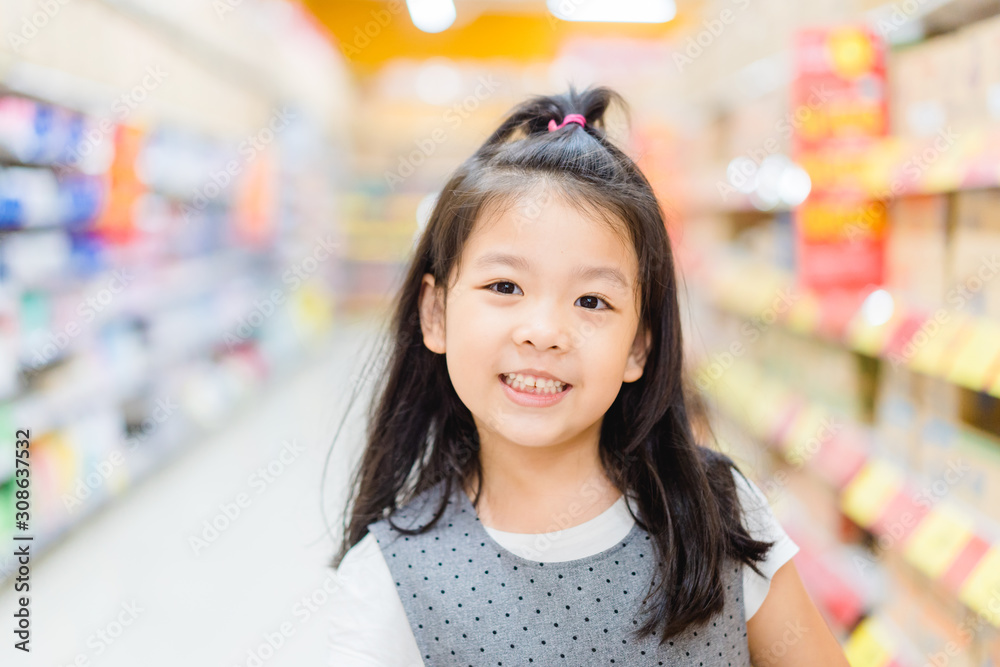 5.8 years old funny little child girl.Little asian girl standing on the trolley and smile when she shopping in supermarket.