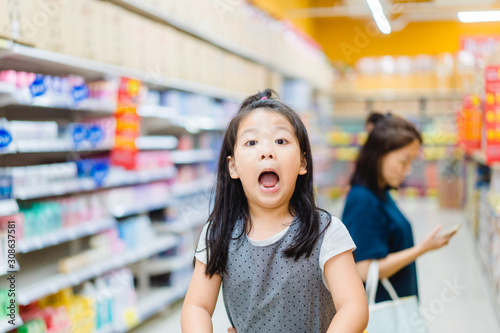 Surprised and excited face of happy little asian girl in supermarket with mom.Little girl open mouth in hypermarket with family.wow emotion in kid.