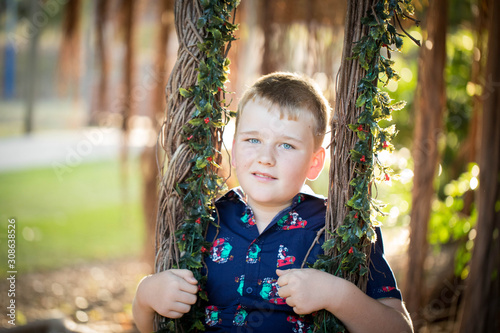 Boy wearing Christmas outfit playing on swing made of fig tree roots covered in mistletoe photo