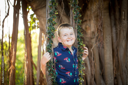 Pre-teen boy in Christmas outfit smiling while playing on fig tree swing covered in mistletoe  photo