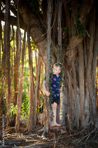 Pre-teen boy in Christmas outfit smiling while playing on fig tree swing covered in mistletoe  photo