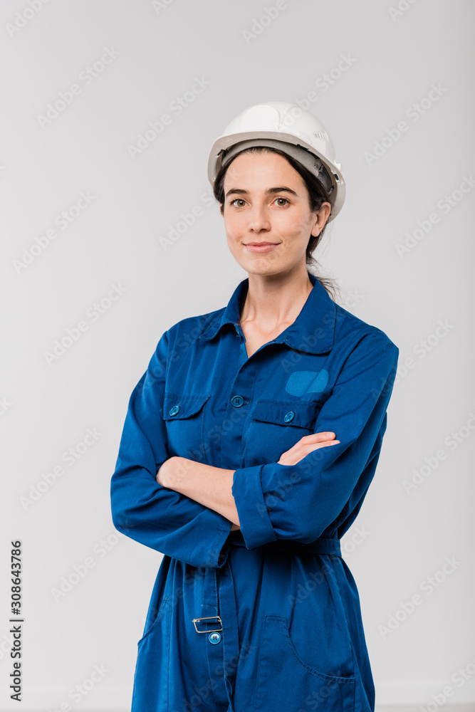 Pretty young cross-armed female engineer in blue workwear and safety helmet Pretty young cross-armed female engineer in blue workwear and safety helmet