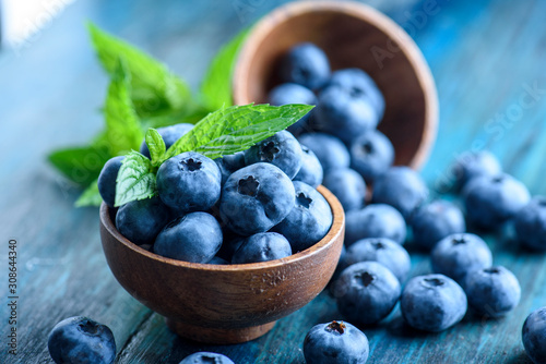 Photo Bowl of fresh blueberries on blue rustic wooden table closeup.