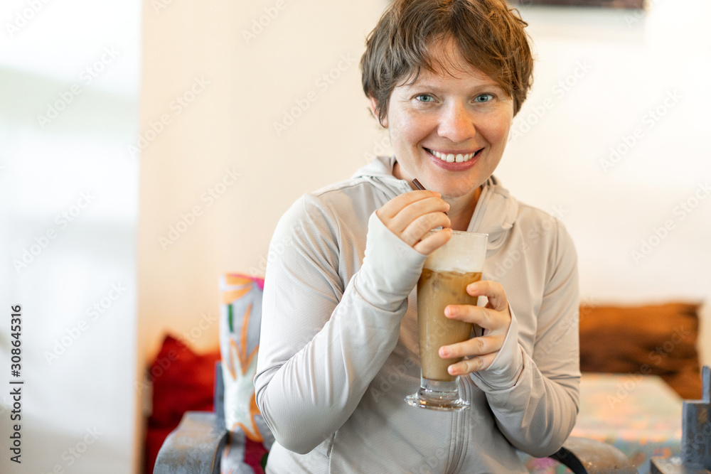 Attractive woman with a short haircut drinking cold coffee from a straw with a smile on her face.