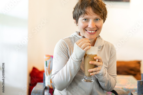 Attractive woman with a short haircut drinking cold coffee from a straw with a smile on her face.