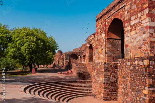 Huge gate structure at a fort made with red sandstone called Talaqi Darwaza near an amphitheatre with blue sky and green trees. A Famous monument known as Purana Qila or Quila in Delhi, India. photo