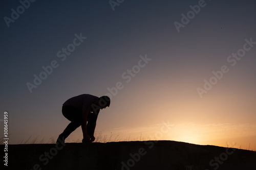 silhouette tying shoe lace at sunset at sunset © robcartorres