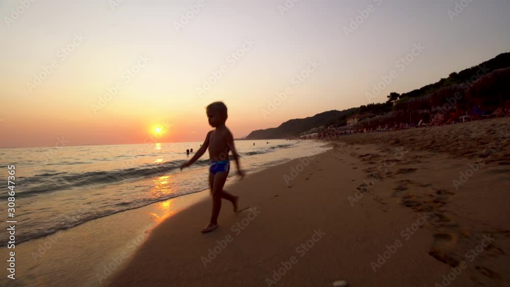 baby boy running on a sand beach toward the camera at sunset