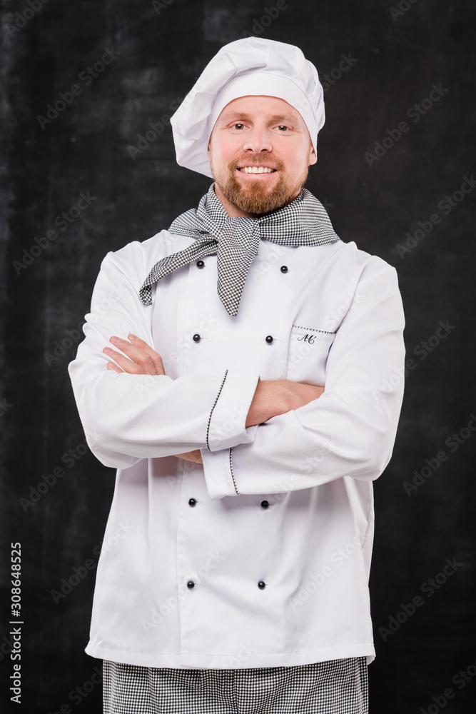 Young smiling male chef crossing arms by chest while looking at you