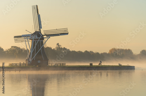 Man with baby stroller running past a windmill on a foggy morning.