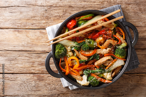 Fototapeta Chinese cuisine stir fry pork with vegetables and sesame seeds close-up in a pan