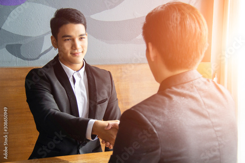 Bussiness done deal! Two modern asian bussinessman are shaking hands and smile while their meeting.