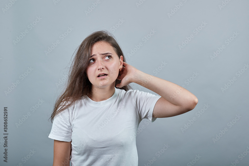 Young lady in white t-shirt over isolated wall holds her palm near her neck and listening to gossips with ear Young lady in white t-shirt over isolated wall holds her palm near her neck and listening to gossips with ear