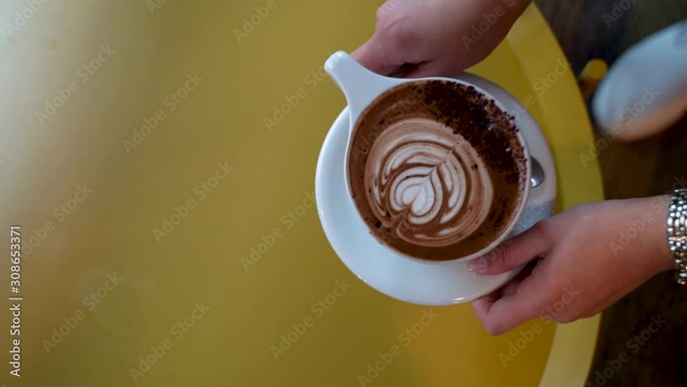 Grabbing a mocha with beautiful latte art in a ceramic cup from a coffee table in a coffee shop. Grabbing a mocha with beautiful latte art in a ceramic cup from a coffee table in a coffee shop.