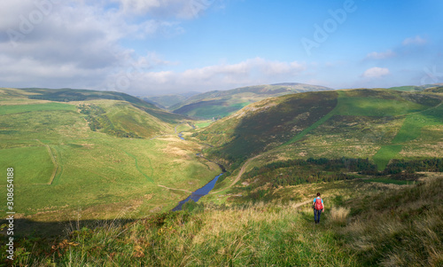 A female hiker walking towards Coquet river at Upper Coquetdale in Northumberland, England.