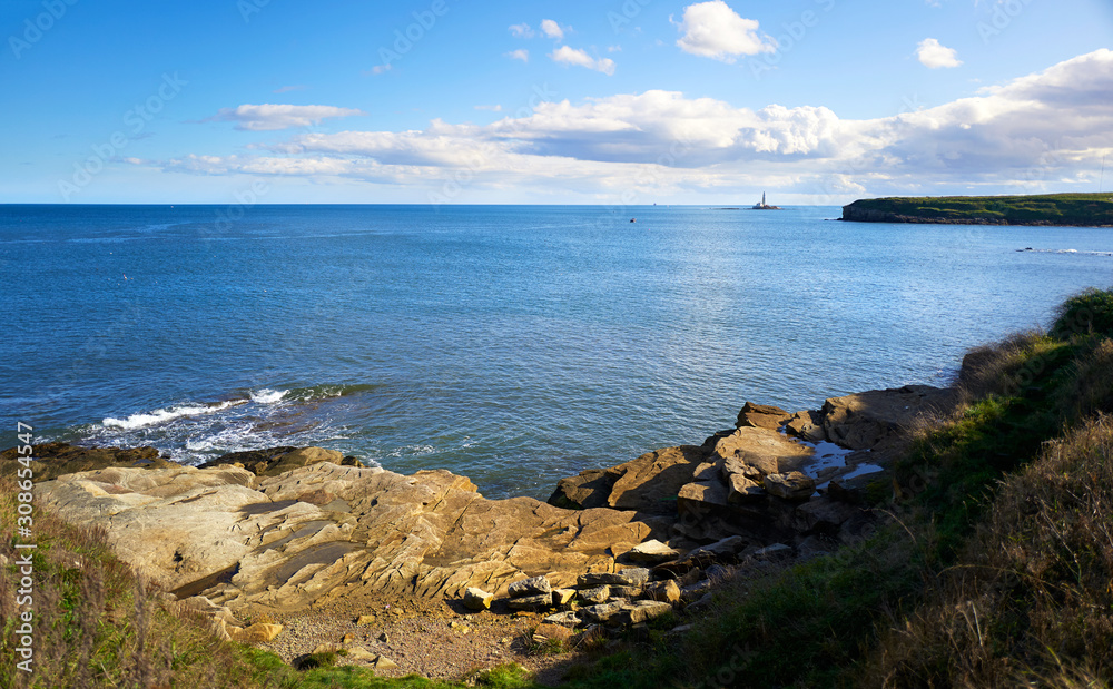 The rocky coastline of Seaton Sluice with St Mary's Lighthouse out at sea in the distance.