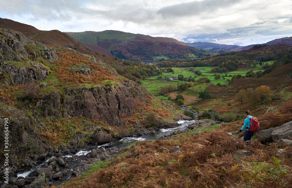 A hiker walking down a rocky mountain trail towards Grasmere in Autumn in the English Lake District.