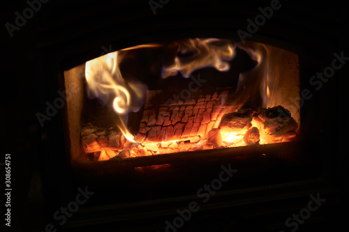 A closeup of a log burning fire with the warm glow of flames in a black stove.