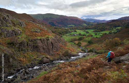 A hiker walking down a rocky mountain trail towards Grasmere in Autumn in the English Lake District.