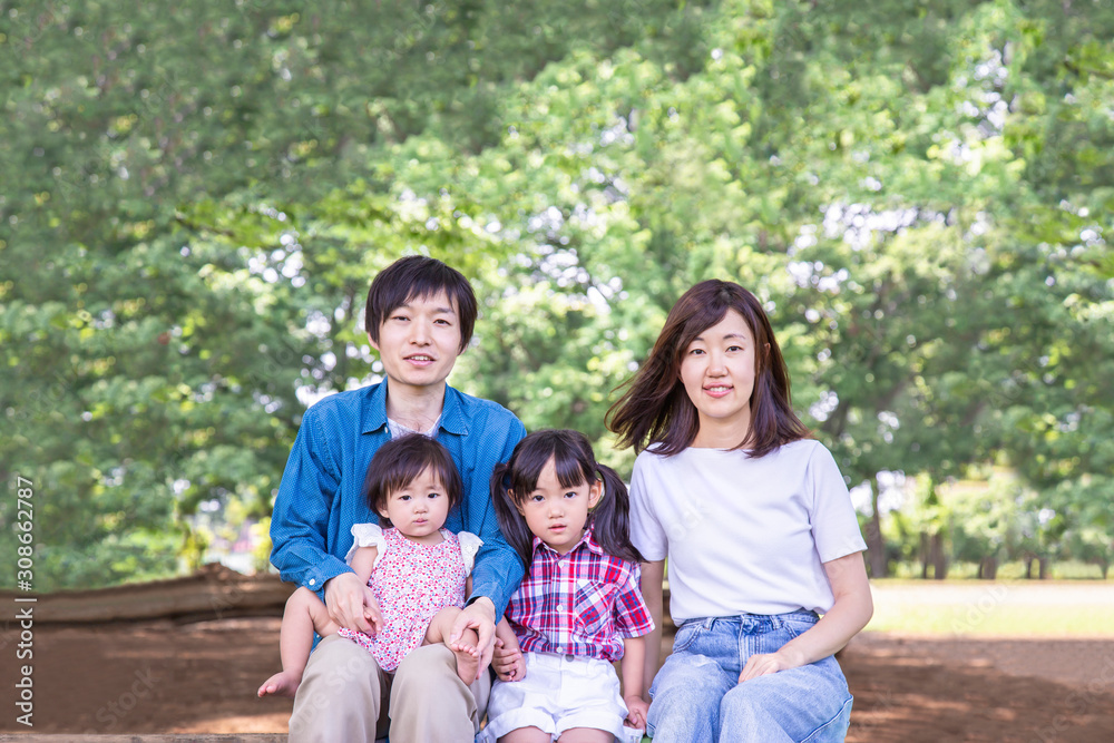 新緑の公園を背景に座る家族4人。幸せ、愛情イメージ