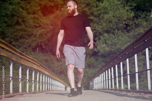 one caucasian bearded young man in black jersey walking along wooden bridge in park during sport training fitness activity
