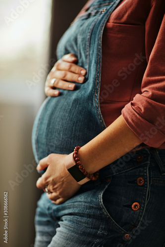 Close up of pregnant caucasian pregnant woman standing next to window and touching belly. Baby is kicking.