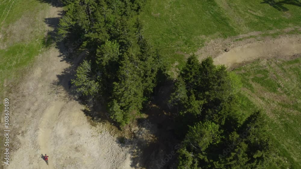 Aerial view of three mountain bikers on a sharp turn at Kope downhill park Slovenia during the summer, Drone Tracks from above Aerial view of three mountain bikers on a sharp turn at Kope downhill park Slovenia during the summer, Drone Tracks from above