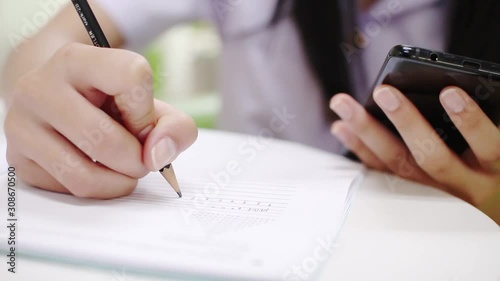 Girl student holding pen and writing in notebook. Close up,And use the phone 