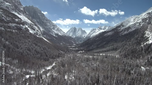 Flying with drone over high altitude mountain valley (Shuangqiao) with blue sky, snowy forest, and mountains in the background photo