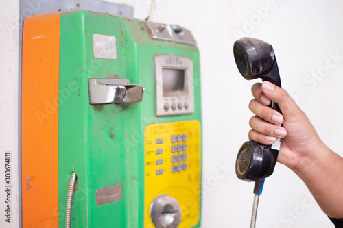 The hand of a person is about to talk by holding a public phone.A rare coin operated public pay telephone in front of a log cabin.