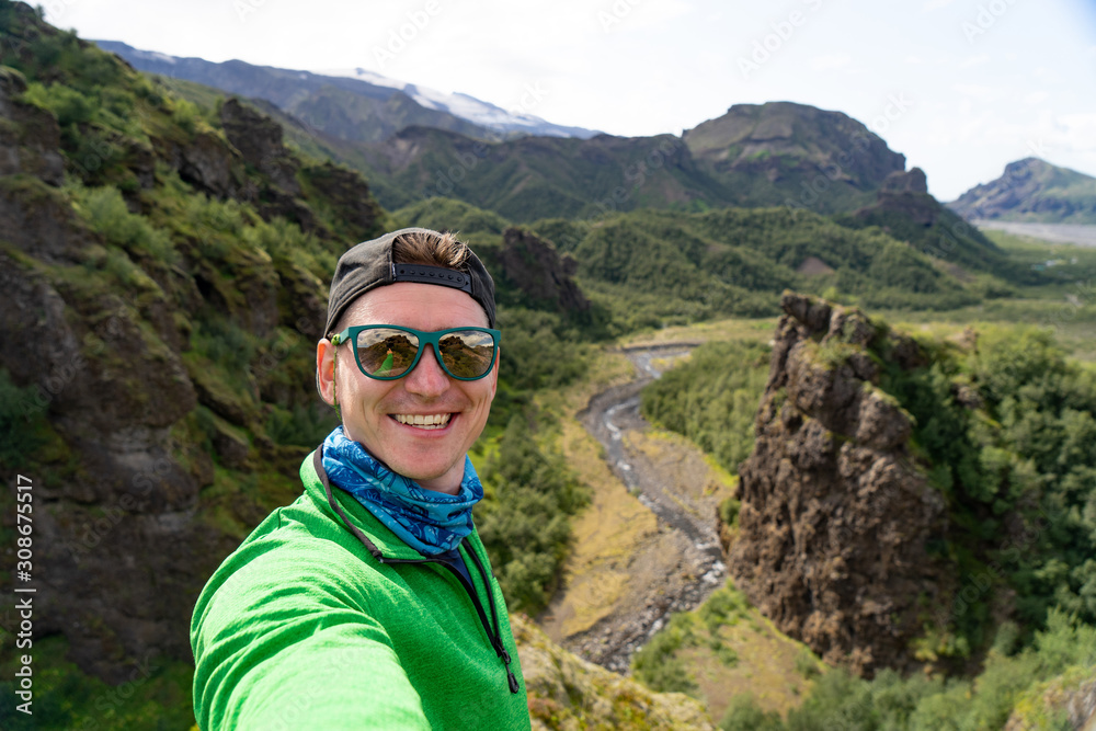 Naklejka premium tourist man on the river and green mountains background takes a picture of Selfie