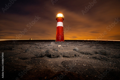 Traditional red and white colored lighthouse against twilight along the Dutch coastline at night