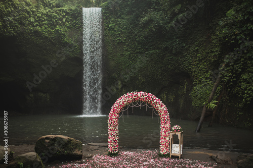 Wedding ceremony on small secret waterfall Tibumana in Bali, Indonesia jungle. Classic round arch with pink and white roses. Unusual destination for wedding. photo