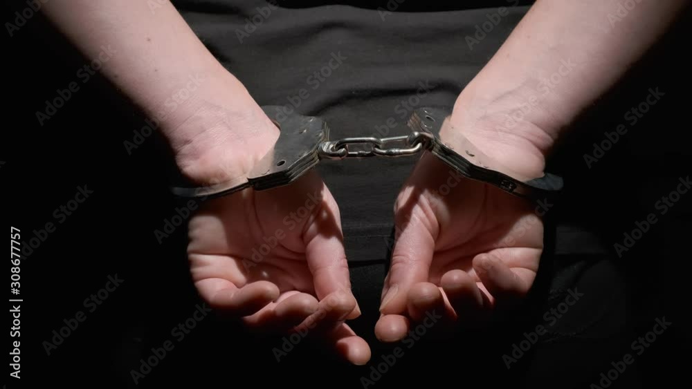 Handcuffs on hands of criminal behind his back on black background close-up. Handcuffs on hands of criminal behind his back on black background close-up.