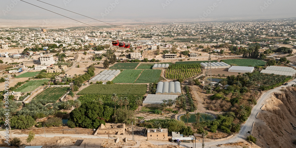 red cable cars going up to the mount of the temptation of jesus in jericho with modern high tech farms in the foreground and the palestinian city in the background